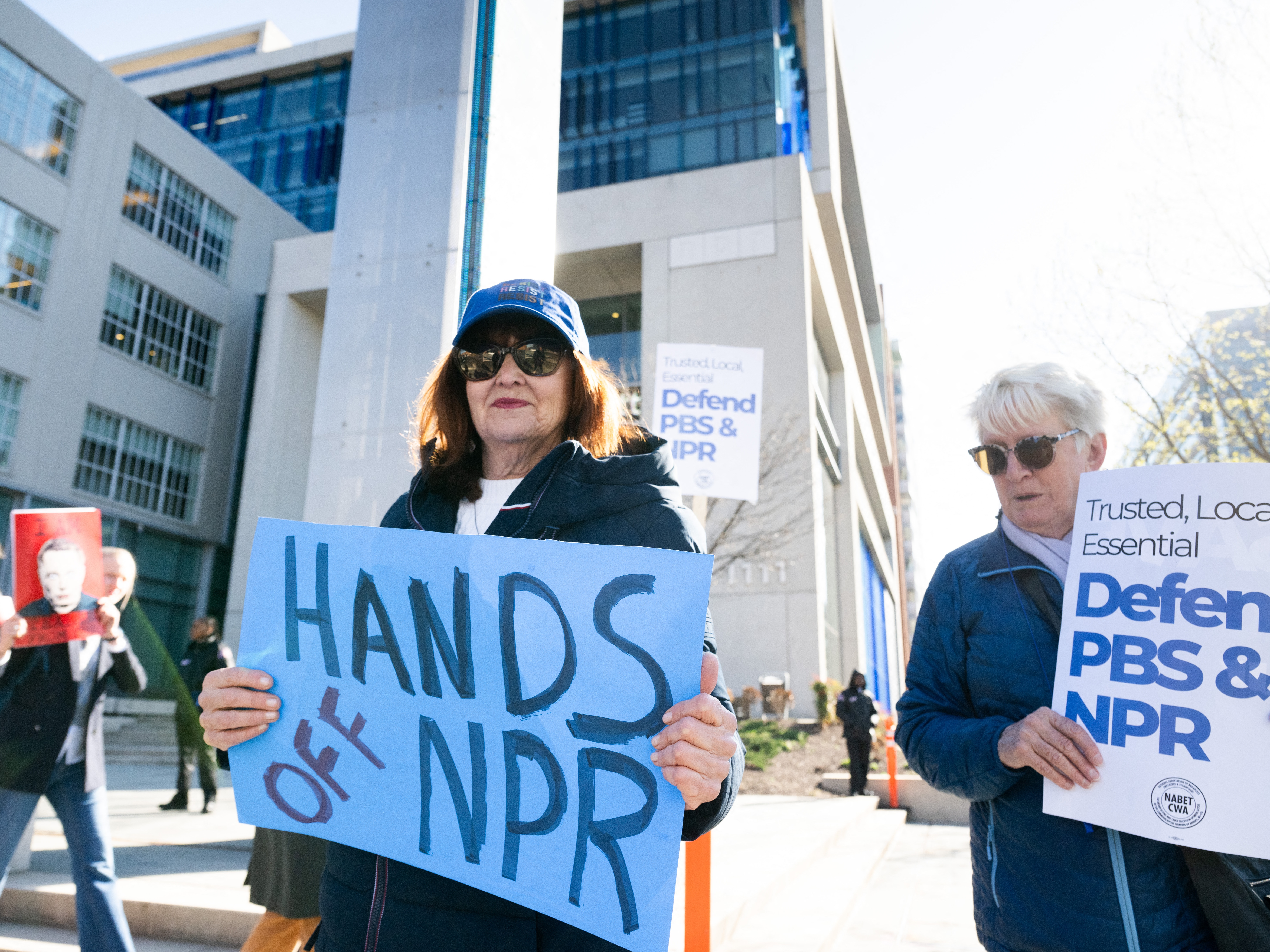 caption: People participate in a rally to call on Congress to protect funding for PBS and NPR outside the NPR headquarters in Washington, DC, on March 26, 2025.