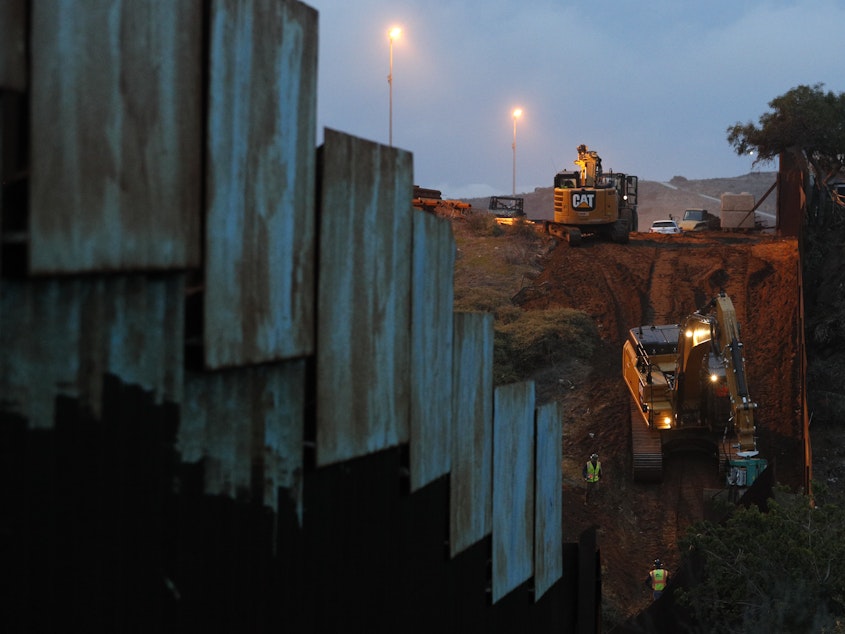 caption: Contractors work to reinforce a section of the U.S. border wall in San Diego where scores of Central American migrants have crossed illegally in recent weeks, shot through the fence from Tijuana, Mexico.