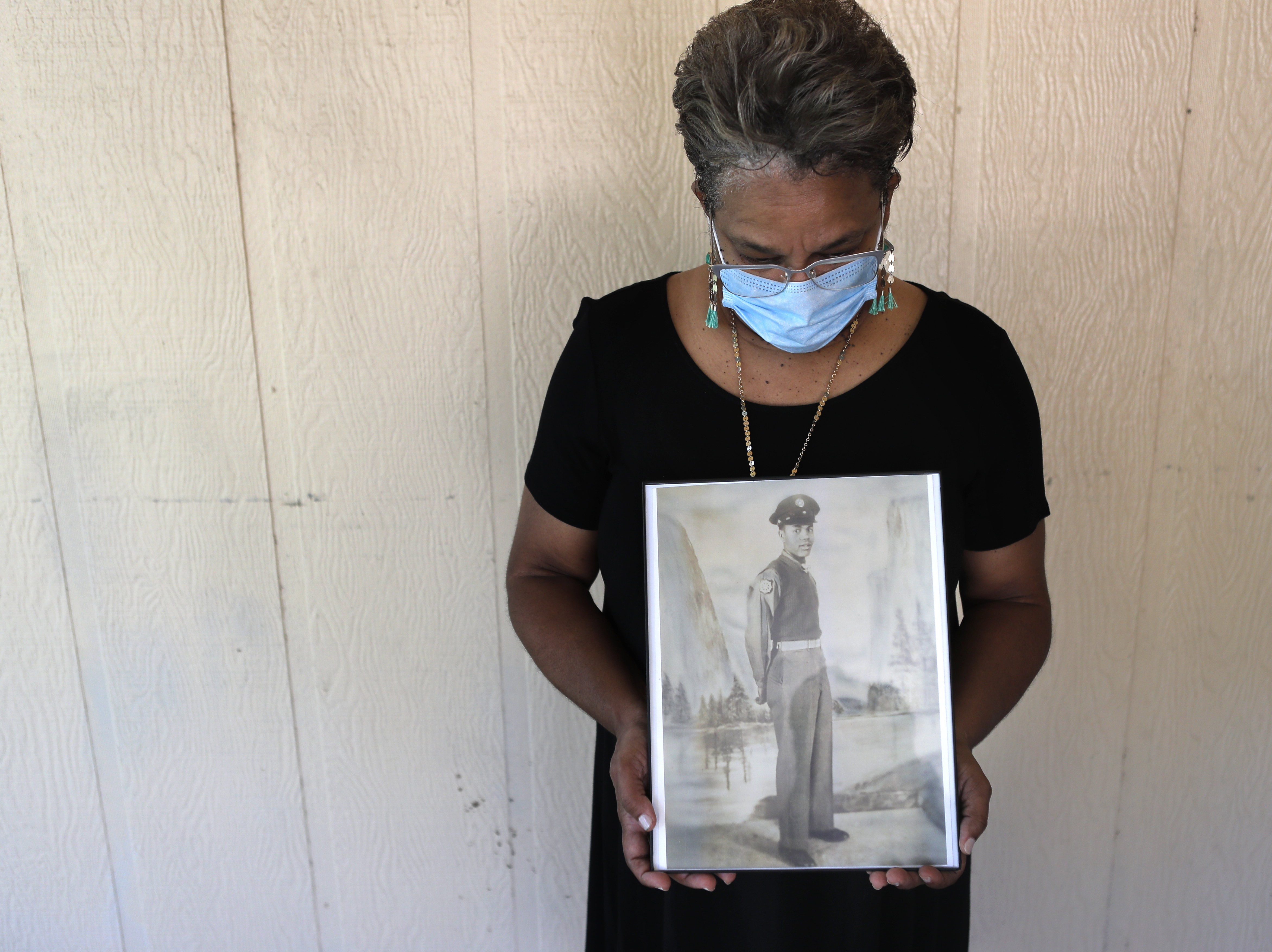 caption: Belvin Jefferson White poses with a portrait of her father Saymon Jefferson, who died from COVID-19, in Baton Rouge, La., in May.