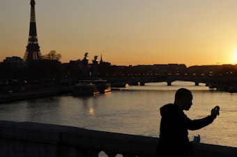 caption: A man takes a picture at sunset with the Eiffel Tower in the background on March 30, 2021. The president of the European Commission says fully vaccinated Americans will be able to visit the EU this summer.
