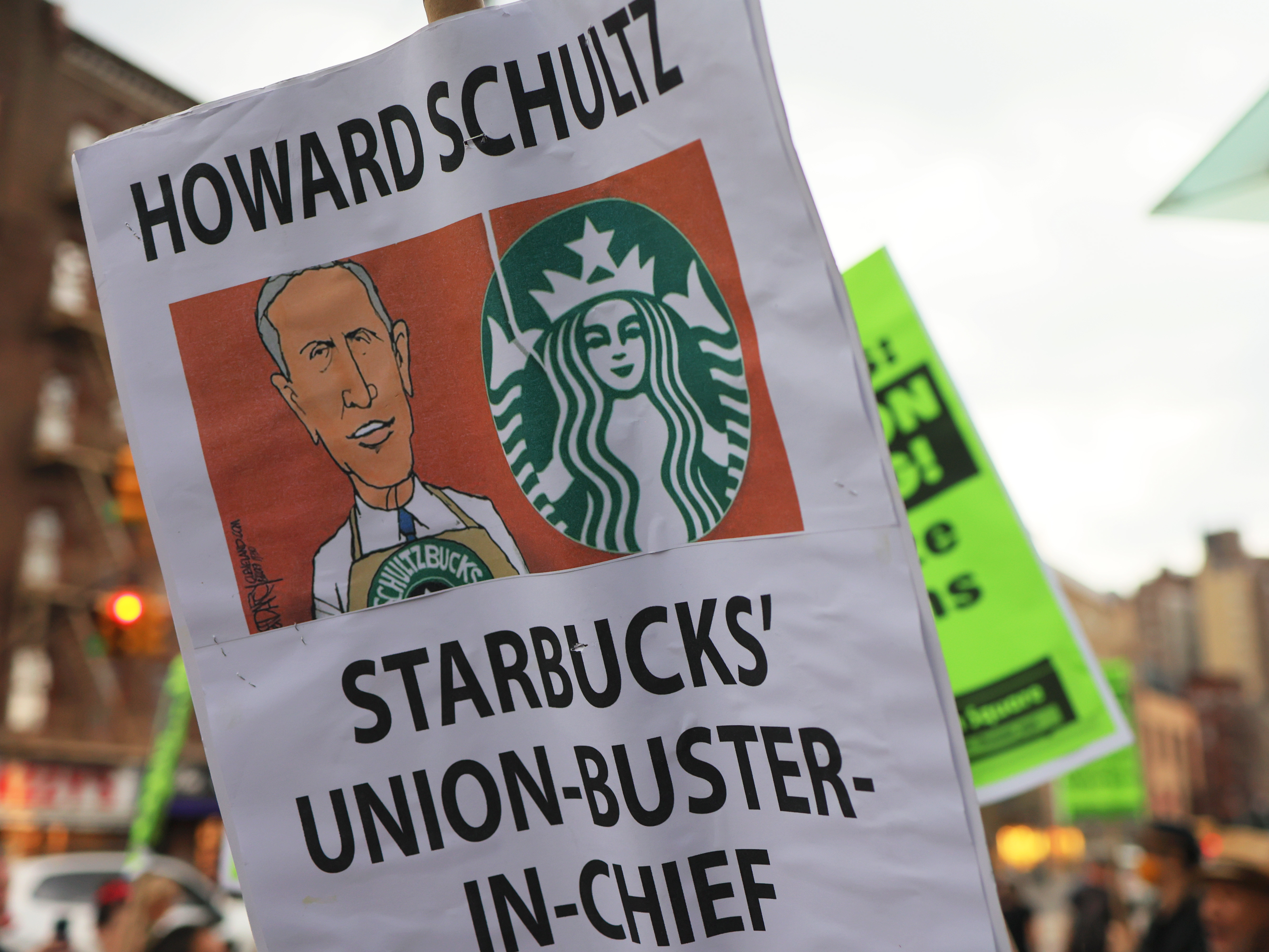 caption: People hold signs while protesting in front of Starbucks on April 14, 2022 in New York City. Activists gathered to protest Starbucks' CEO Howard Schultz anti-unionization efforts and demand the reinstatement of workers fired for trying to unionize.
