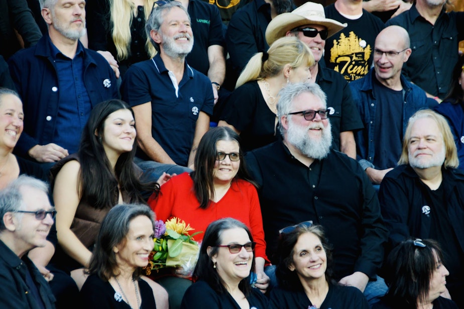 caption: Susie Tennant stands out in red amidst a sea of people dressed mostly in black who showed up to honor her at "A Great Day for Susie" Sept. 25, 2022, outside of MoPop in Seattle. Left of Tennant is her daughter Ella. Right of her is her husband Chris Swenson.