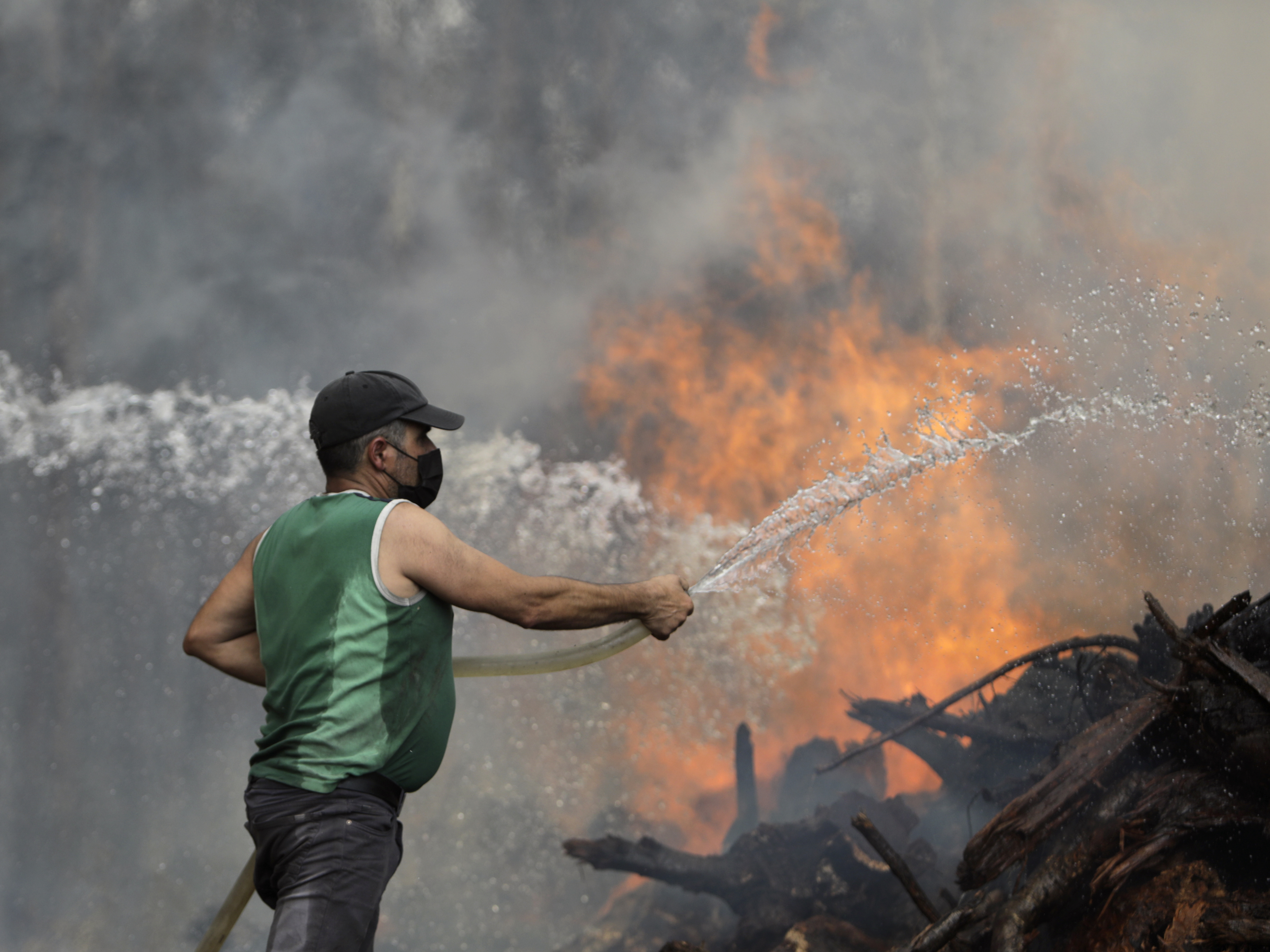 caption: A local resident uses a garden hose to try to stop a forest fire from reaching houses in the village of Figueiras, outside Leiria, central Portugal, Tuesday, July 12, 2022.
