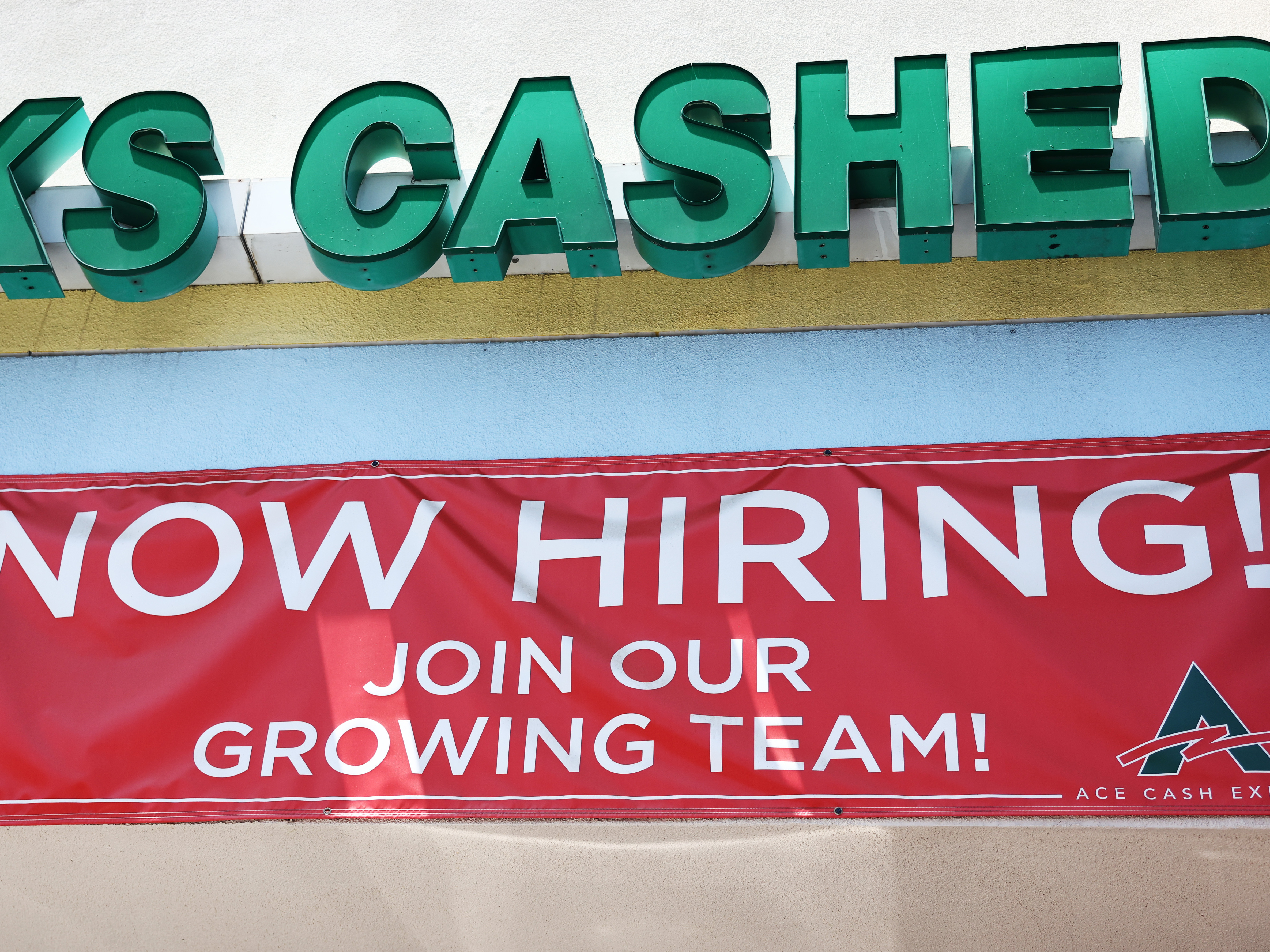 caption: A 'Now Hiring' sign is displayed outside a check cashing shop in Los Angeles on June 2, 2023. Employers added 187,000 jobs in August, while the unemployment rate rose to 3.8%.