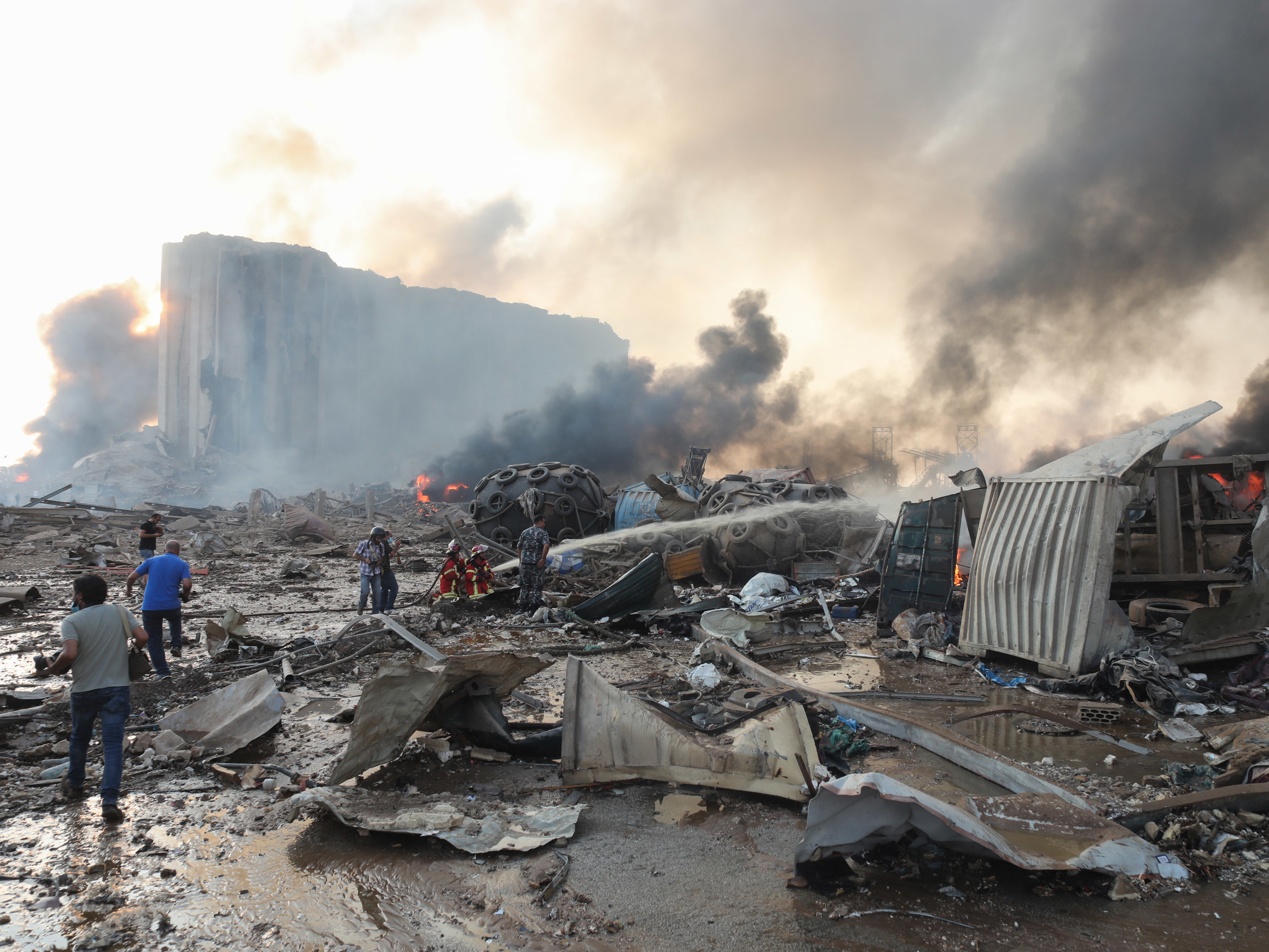 caption: Firefighters extinguish flames at nearby damaged buildings following a large explosion at the Port of Beirut in Lebanon on Tuesday.