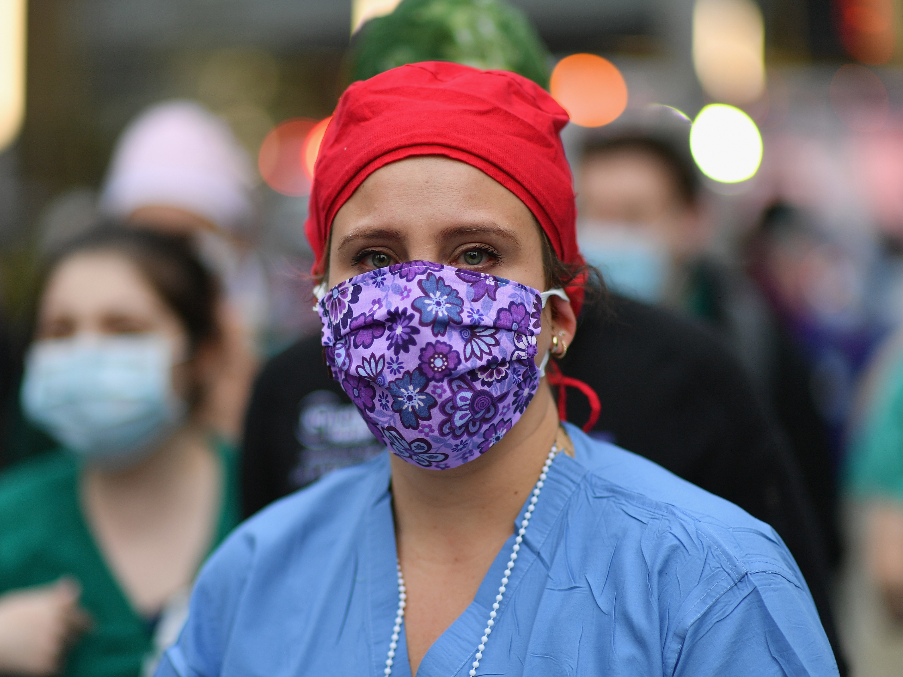 caption: A health care worker looks on as people cheer to show their gratitude to medical staff outside NYU Langone Health hospital in New York City last month.