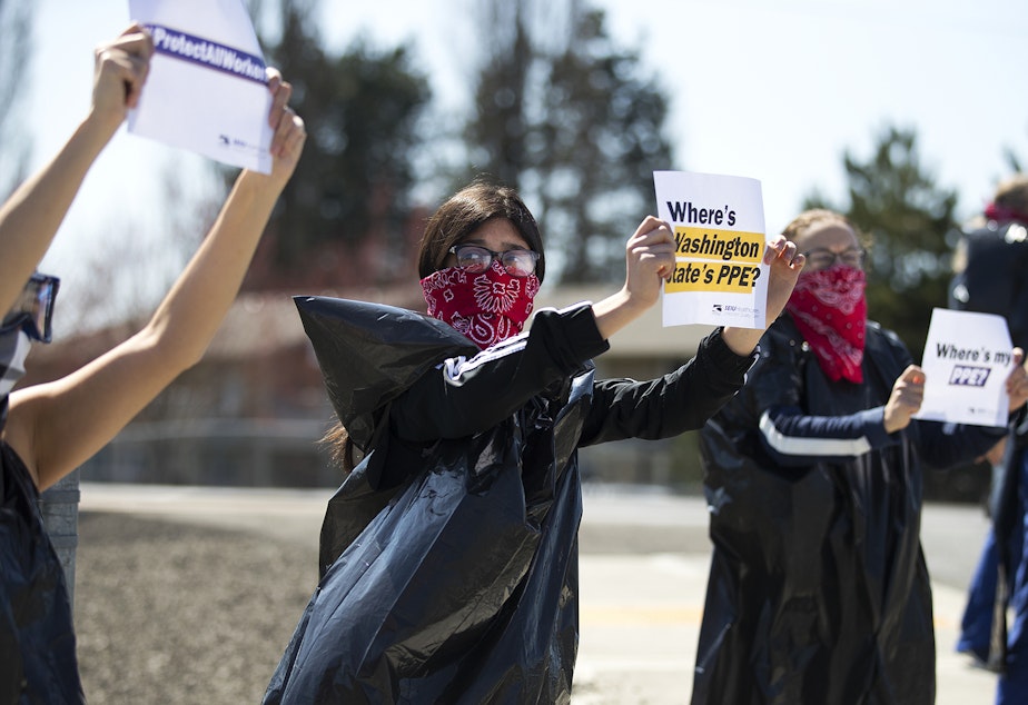 caption: Giselle Uribe-Sayah, 15, wears a garbage bag and handkerchief while joining a nationwide protest demanding PPE for healthcare workers on Thursday, April 9, 2020, outside of Evergreen Health in Monroe.