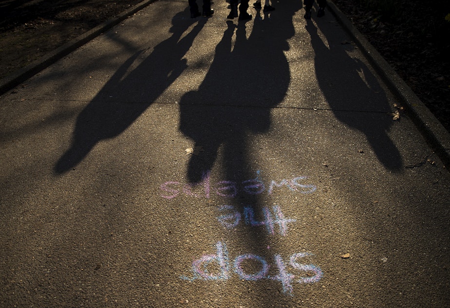 caption: Seattle police officers walk through Denny Park before sweeping unhoused people from the area on Wednesday, March 3, 2021, in Seattle.