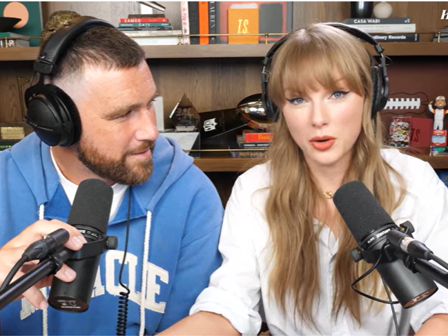 caption: Travis Kelce looks at Taylor Swift during Wednesday's episode of <em>New Heights</em>, the podcast he cohosts with his brother Jason Kelce.