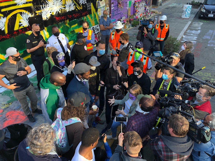 caption: Mayor Jenny Durkan's Chief of Staff, Stephanie Formas, speaks with protester David Lewis after protesters confronted city workers who tried to clear barriers at 5:30 AM on June 26, 2020. Also present is Fire Chief Harold Scoggins and SDOT head Sam Zimbabwe.
