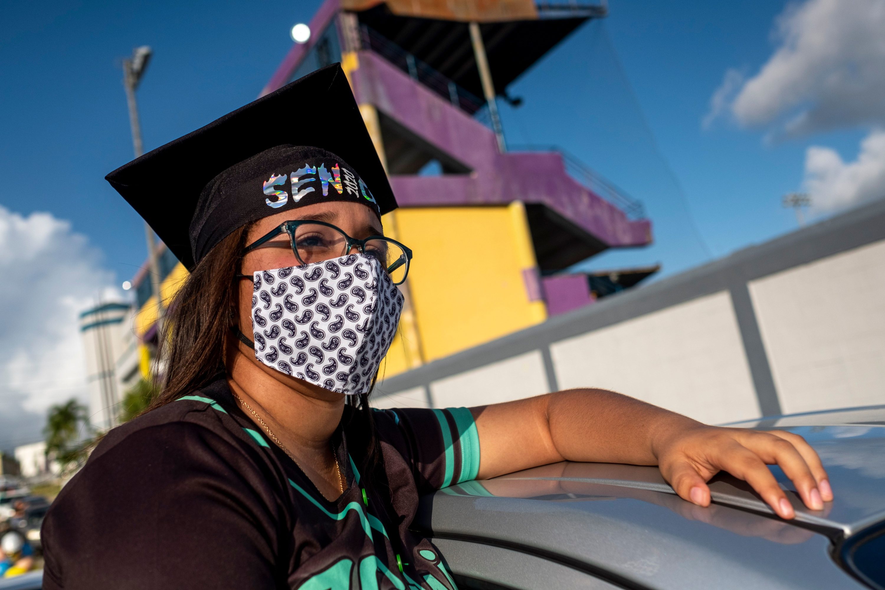caption: A graduating student from the Ramon Power Y Giralt High School attends a symbolic graduation from inside her car to maintain social distance at a parking lot in Las Piedras, Puerto Rico, on May 13, 2020. (RICARDO ARDUENGO/AFP via Getty Images)