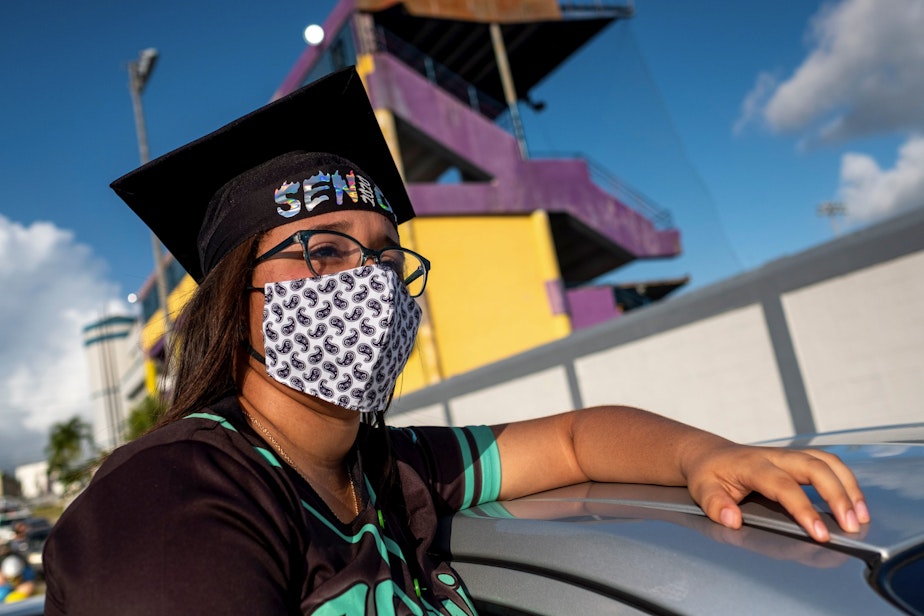 caption: A graduating student from the Ramon Power Y Giralt High School attends a symbolic graduation from inside her car to maintain social distance at a parking lot in Las Piedras, Puerto Rico, on May 13, 2020. (RICARDO ARDUENGO/AFP via Getty Images)