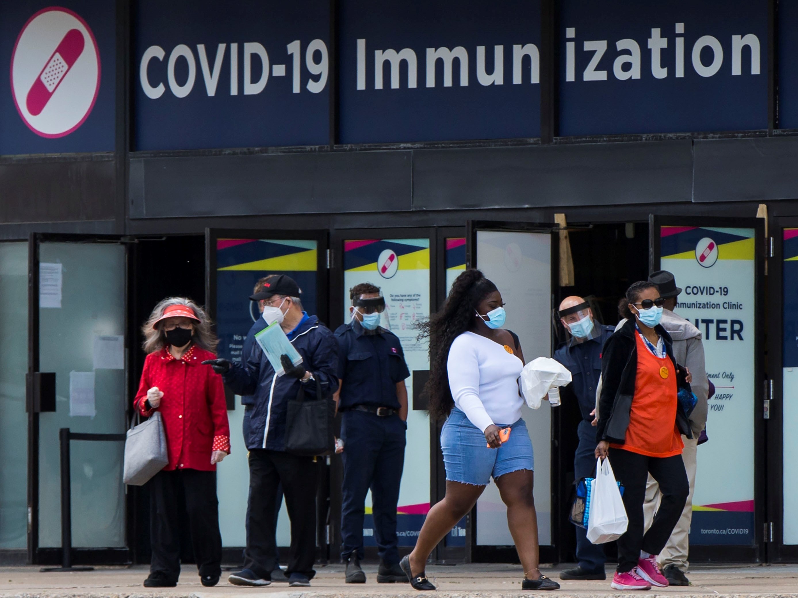 caption: Canada's National Advisory Committee on Immunization is recommending allowing people to mix COVID-19 vaccine doses. Here, people walk past a vaccination clinic this week in Toronto.