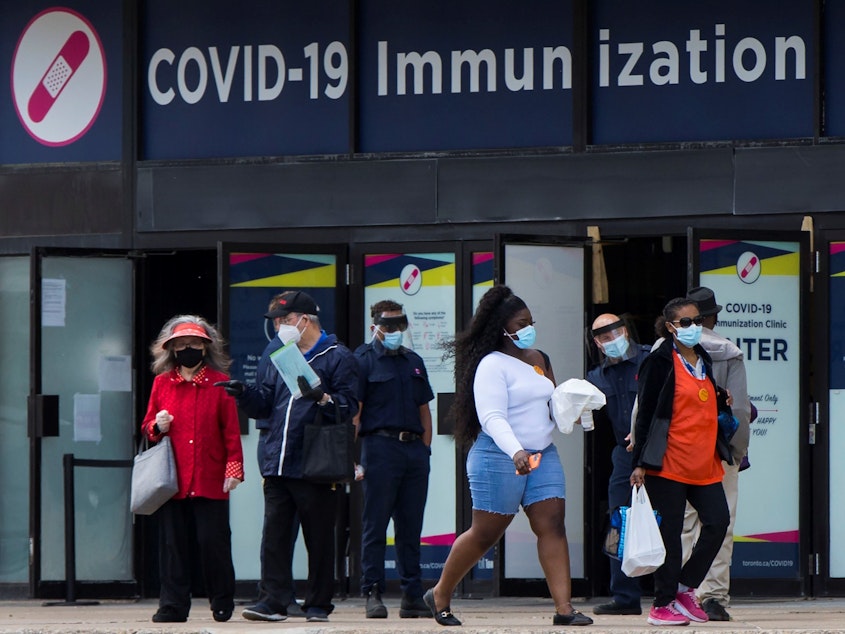 caption: Canada's National Advisory Committee on Immunization is recommending allowing people to mix COVID-19 vaccine doses. Here, people walk past a vaccination clinic this week in Toronto.