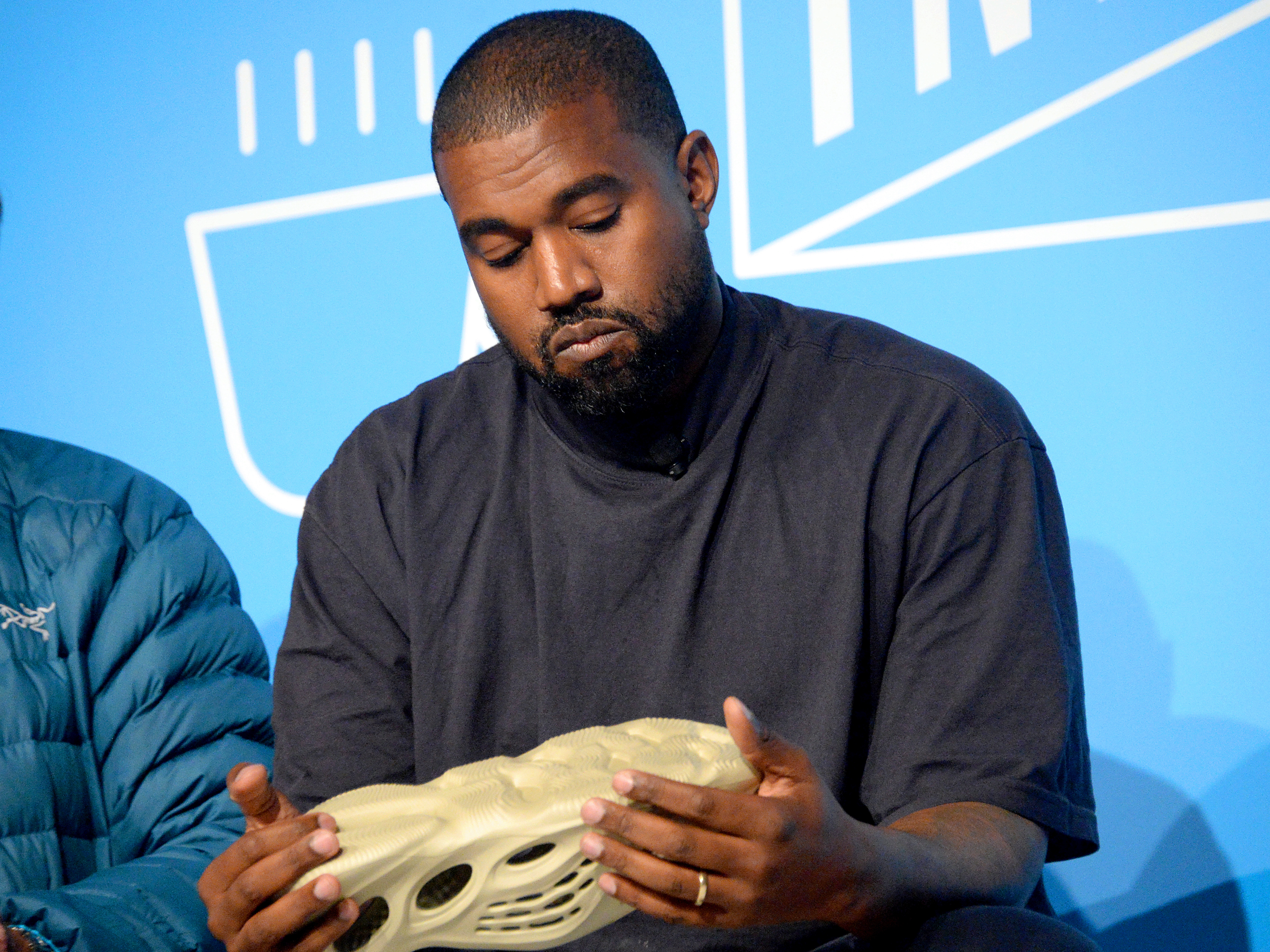 caption: Kanye West holds a Yeezy shoe as he speaks on stage at the "Kanye West and Steven Smith in Conversation with Mark Wilson" at the on Nov. 7, 2019 in New York City.