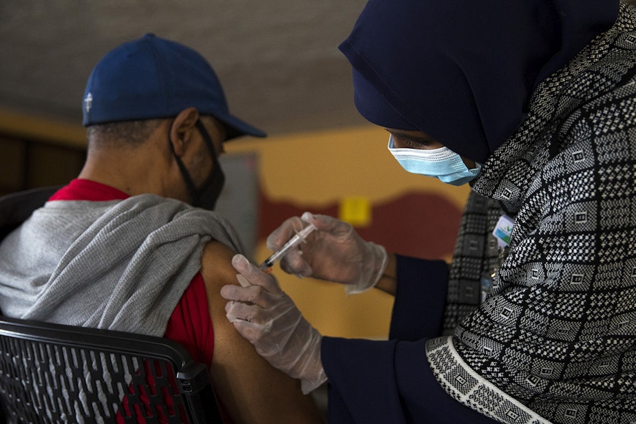 caption: Registered nurse Hamdi Abdi, right, administers the first dose of the Moderna Covid-19 vaccine for Charles Jackson, left, on Wednesday, February 3, 2021, during a vaccine clinic set up by the Somali Health Board in partnership with the Othello Station Pharmacy and Brighton Apartments to vaccinate 100 seniors in the community on at the apartment complex along Rainier Avenue South in Seattle. 