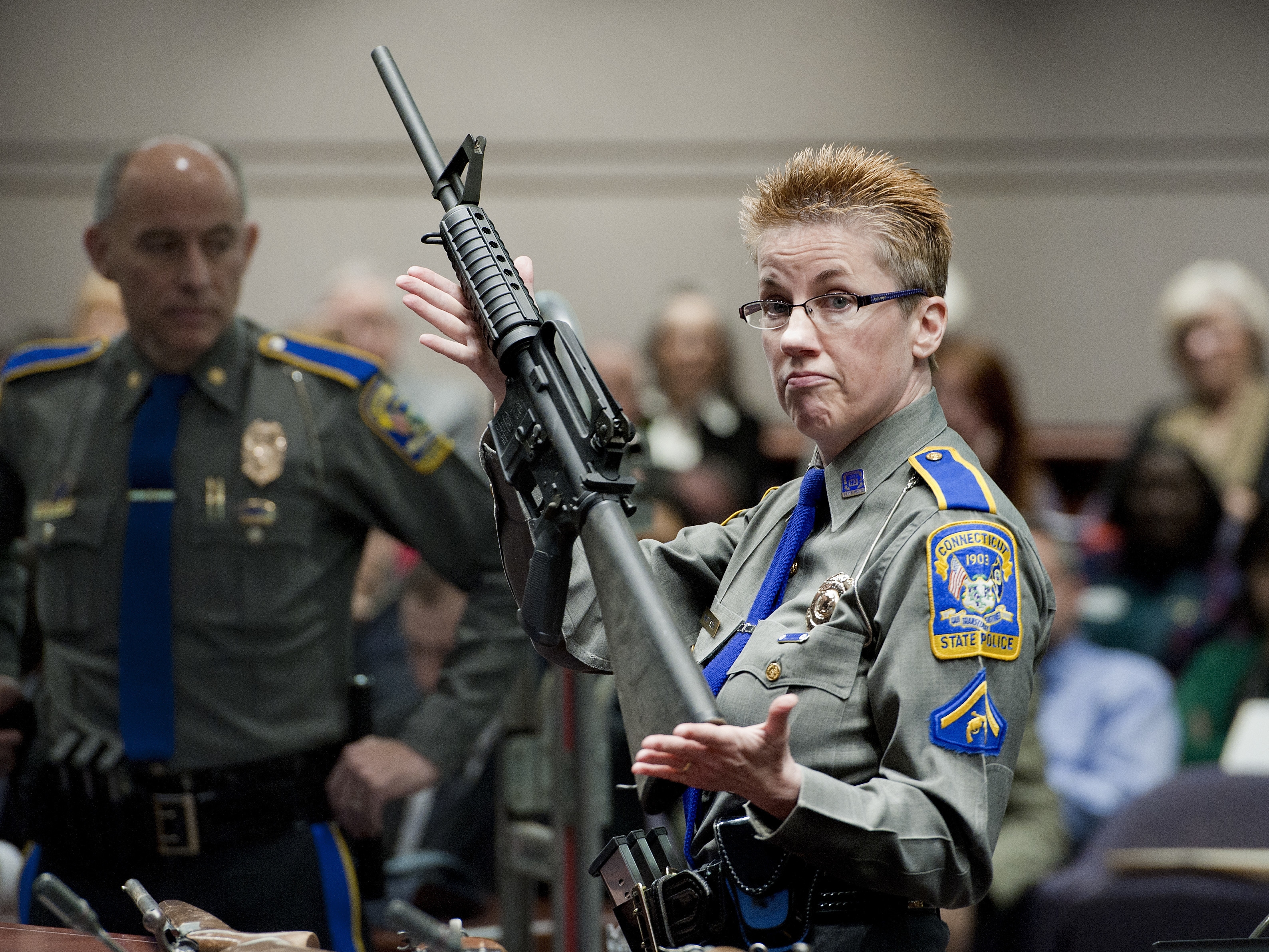 caption: Connecticut State Police Detective Barbara J. Mattson holds a Bushmaster AR-15-style rifle, the same type of gun used in the Sandy Hook shooting, during a 2013 hearing in Hartford, Conn. The gun-maker Remington is being sued by the families of the victims.