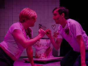 caption: Andrew Caira (left) and Adam Parbhoo (right) star in a performance of <em>Saw the Musical: The Unauthorized Parody of Saw</em> at Manhattan's AMT theater.