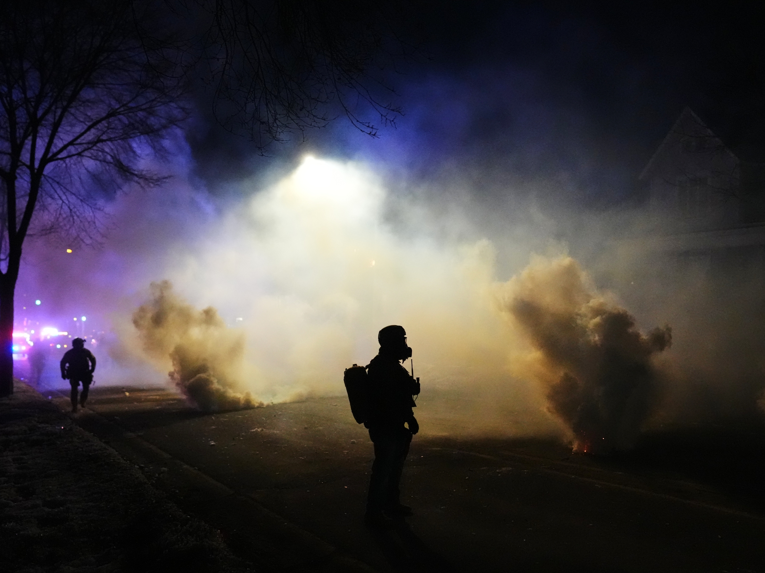 caption: Law enforcement officers stand amid tear gas at the scene of a shooting Wednesday in Minneapolis.