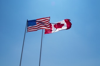 caption: Canada and American flags fly side by side