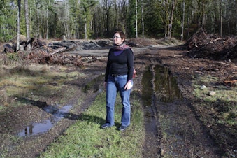 caption: Reporter Carolyn Adolph stands on a development site near Black Diamond, WA. Her fellow reporter Joshua McNichols is behind the camera.