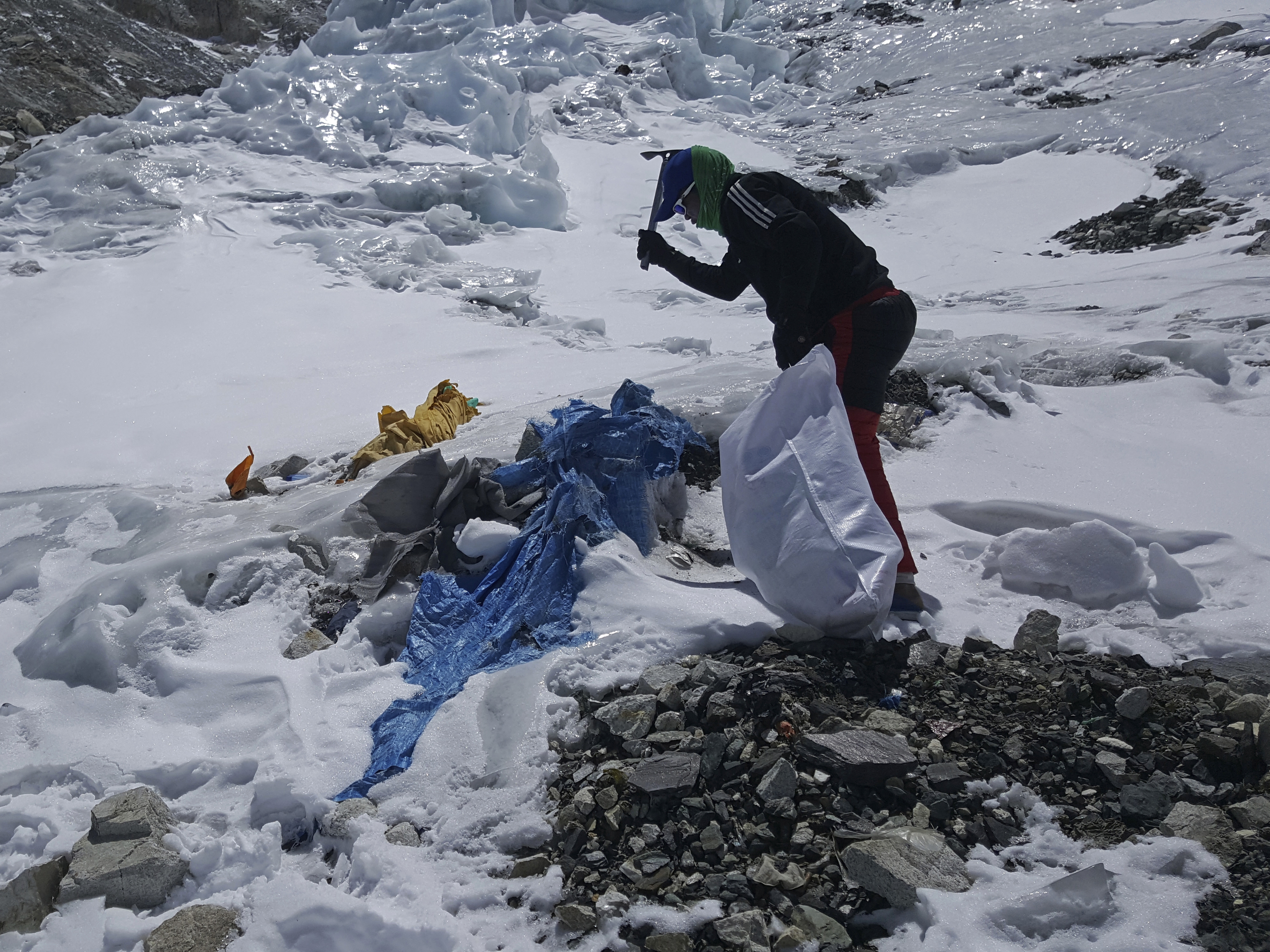 caption: A member of a Nepal government-funded team uses a spade to remove frozen trash on Mount Everest in Nepal in 2021. In the seven decades since Mount Everest was first conquered, thousands of climbers have scaled the peak, and many have left behind more than just their footprints.