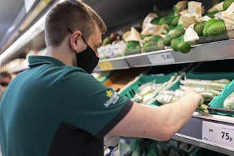 caption: A uniformed member of staff wearing a face covering sorts through fresh produce in British supermarket chain Morrisons last month in Leeds, United Kingdom.