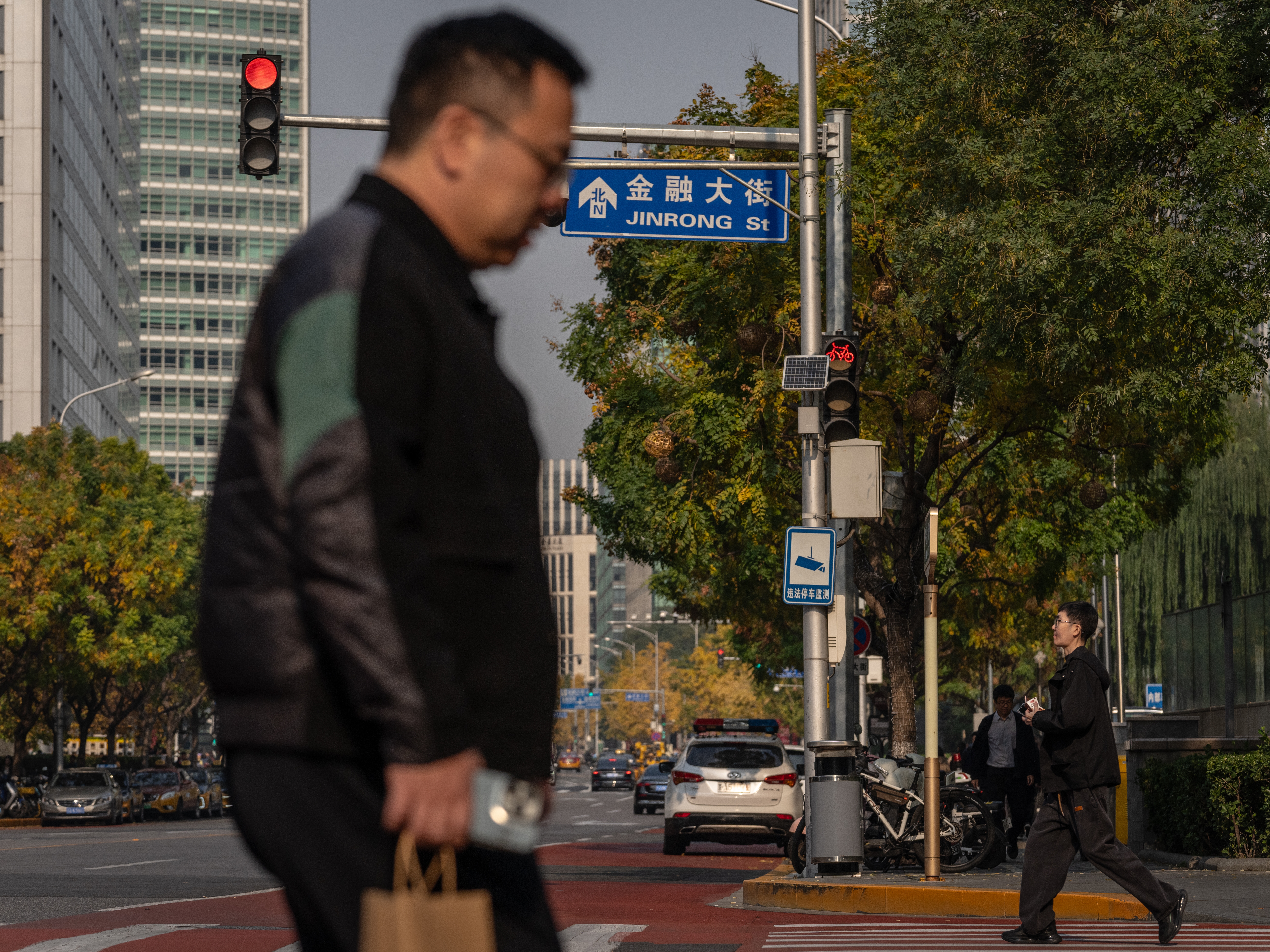 caption: Pedestrians cross a road on Financial Street in Beijing, China, on Thursday. When Donald Trump first started a trade war with China in 2018, Beijing found itself on the back foot and unsure of how to respond. This time President Xi Jinping is better prepared for a fight, even as he has more to lose.