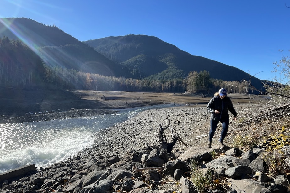 caption: Seattle Public Utilities' Julie Crittenden walks by a mostly dry portion of the Chester Morse Reservoir on the Cedar River in the Washington Cascades on Nov. 17, 2023.