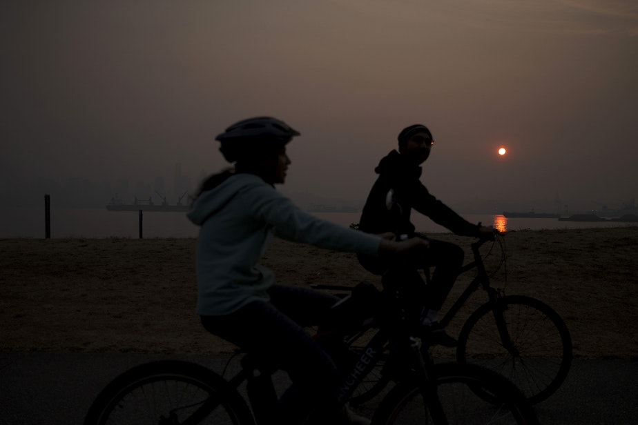 caption: Cyclists ride along Harbor Avenue Southwest as the sun rises over a smoky Seattle on Friday, Sept. 11, 2020. A massive plume of smoke from wildfires burning in California and Oregon made it's way into the area overnight on Thursday.