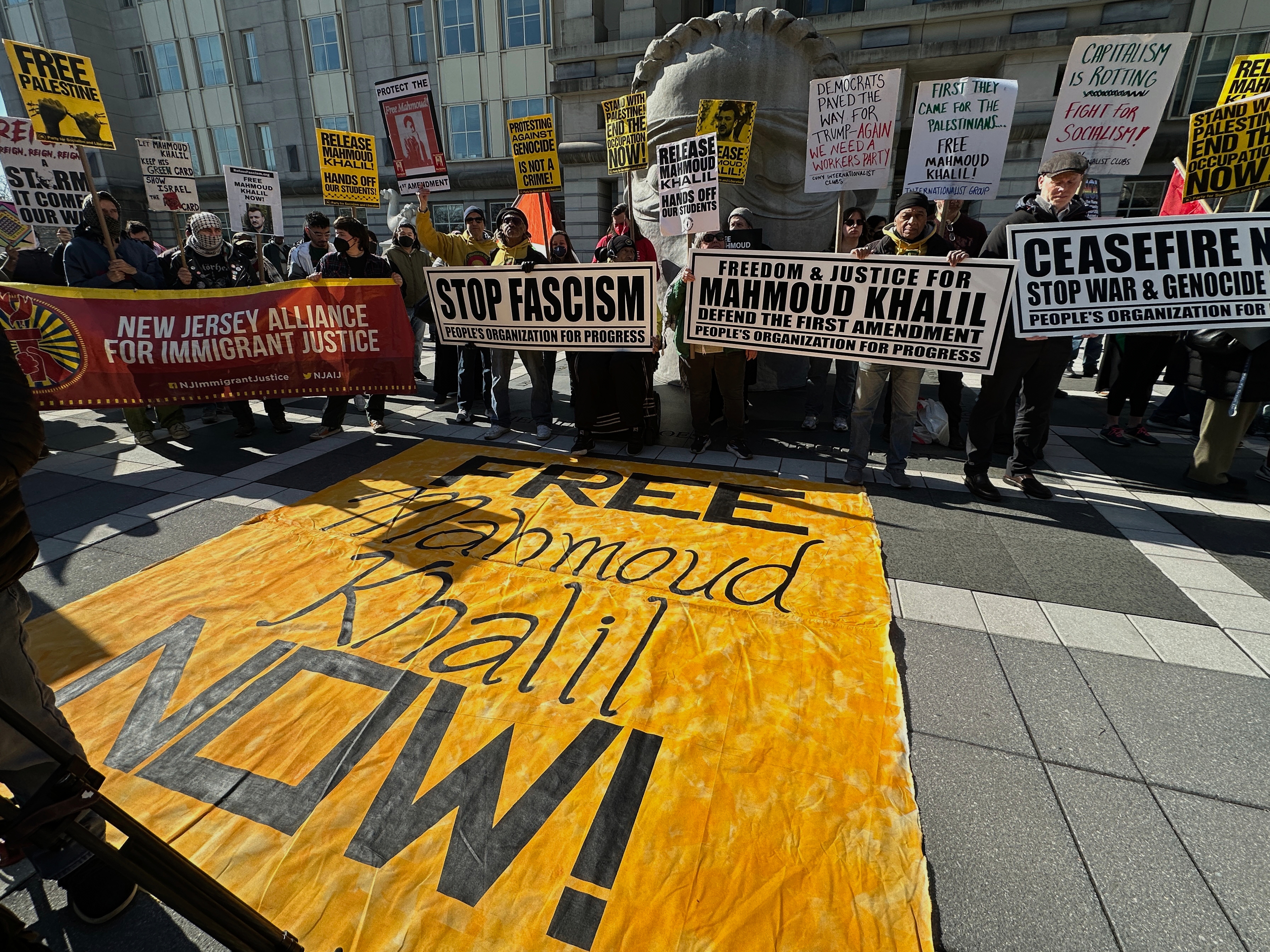 caption: Pro-Palestinian protesters demanding the release of Columbia University graduate student Mahmoud Khalil stand outside his immigration court hearing in Newark, N.J., on Friday, March 28, 2025.