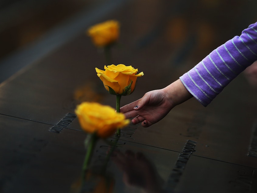 caption: A child reaches out to touch a flower adorning the 9/11 Memorial on the name of a veteran killed on Sept. 11, 2001.