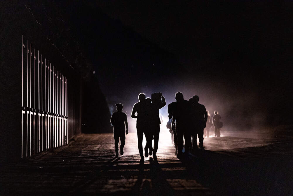 caption: Migrants walk along the border fence after crossing into the U.S. from Mexico through an abandoned railroad. (Qian Weizhong/VCG via Getty Images)