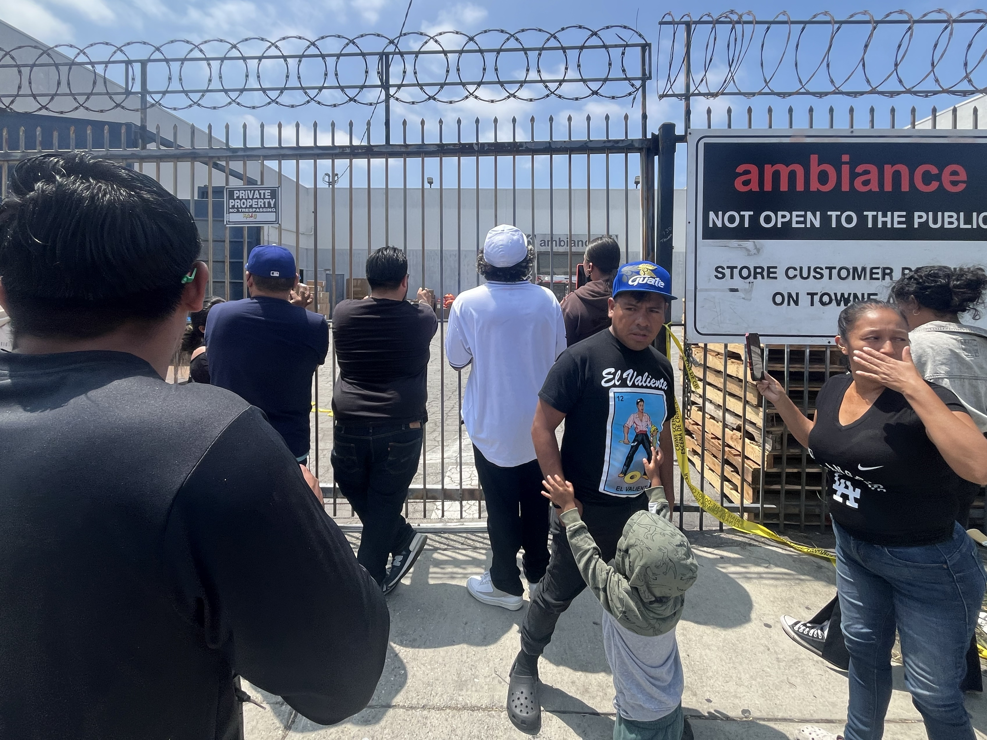 caption: People gather in front of Ambiance Apparel after several employees were taken into custody by federal agents in the Fashion District in downtown Los Angeles on Friday.