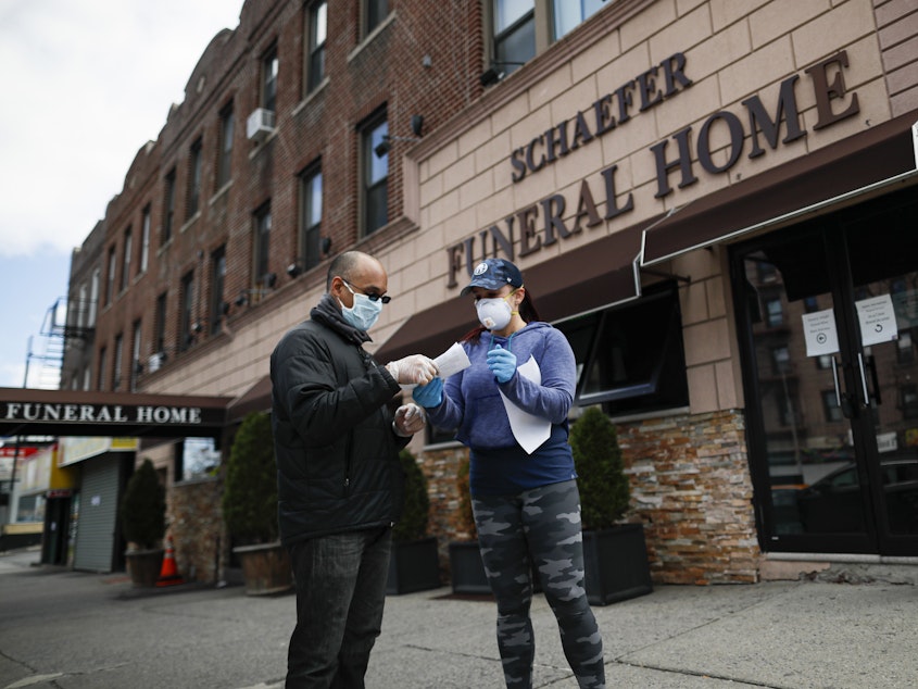 caption: Employee Gina Hansen (right), hands documentation to a client outside Daniel J. Schaefer Funeral Home in Brooklyn, on April 2, 2020.