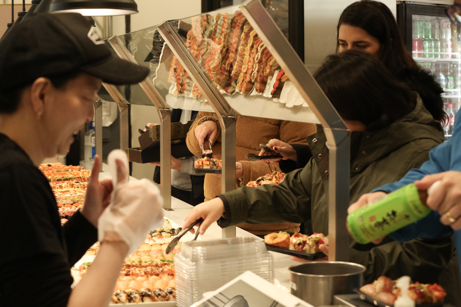 caption: Customers of FOB Sushi in downtown Seattle, line up to pick up their orders during a busy morning in December 2024.