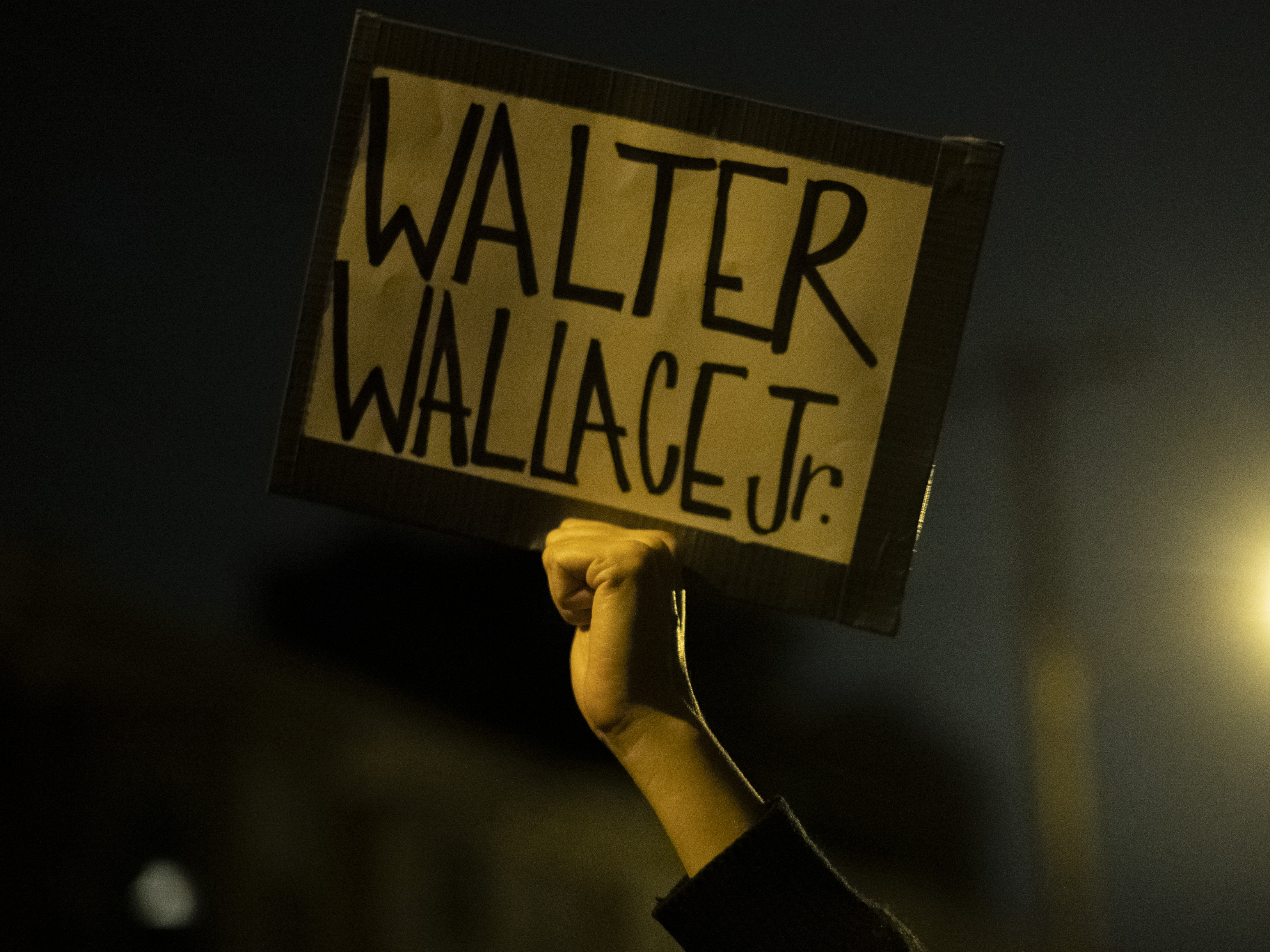 caption: A demonstrator holds a placard with Walter Wallace Jr.'s name on it during a protest near the location where he was killed by two police officers in Philadelphia.