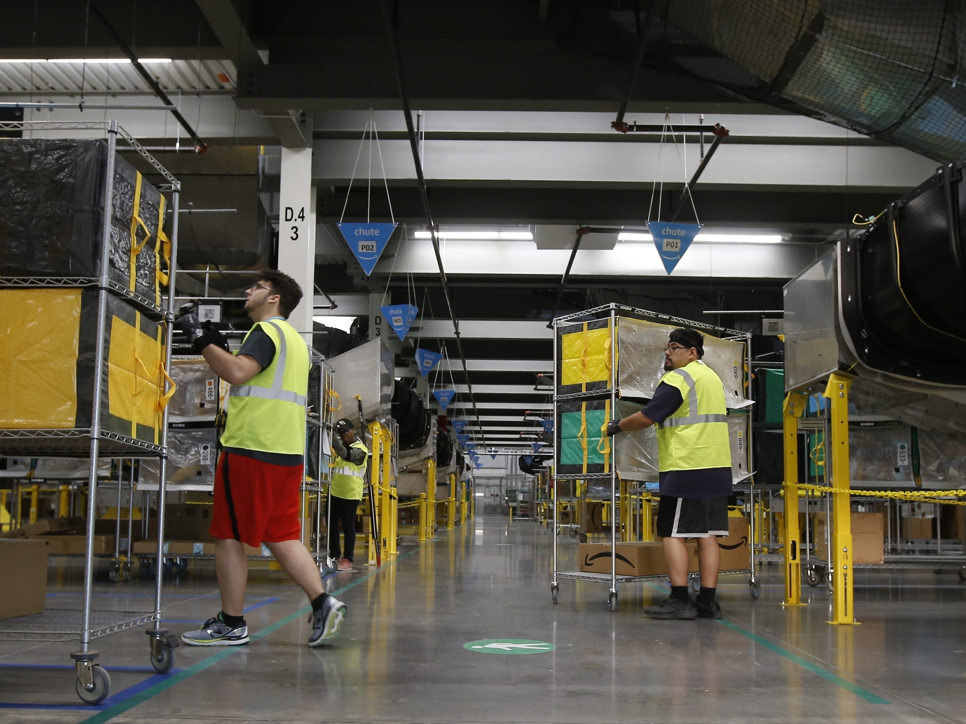 caption: In this Dec. 17, 2019, file photo, Amazon workers move containers to delivery trucks at an Amazon warehouse facility in Goodyear, Ariz.