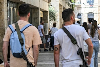 caption: Israeli men, armed with U.S.-made M16 automatic assault rifles, walk in a shopping center in Jerusalem on Oct. 25, amid the ongoing battles in the Gaza Strip between Israel and Hamas.