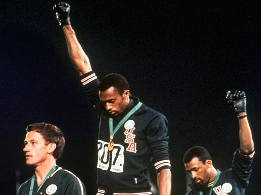 caption: Australian silver medalist Peter Norman (left) stands on the podium as Americans Tommie Smith (center) and John Carlos raise their gloved fists in a human rights protest at the 1968 Summer Olympics in Mexico City.
