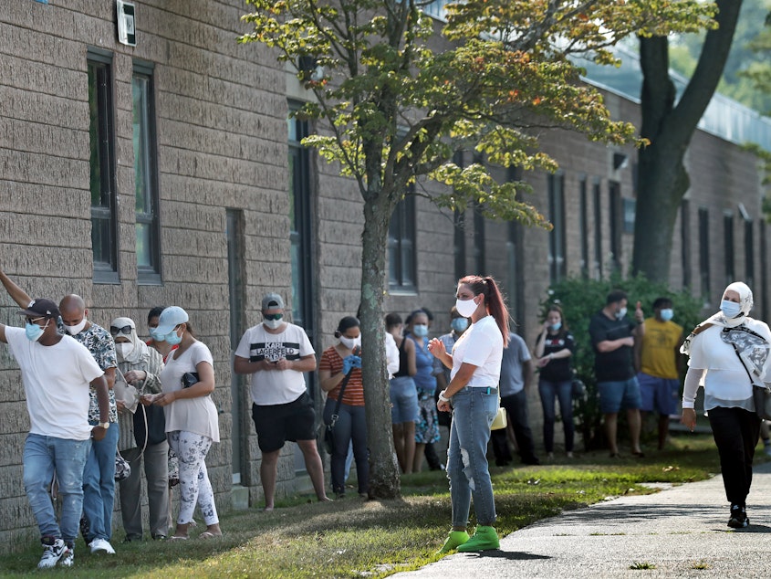 caption: People wait in the shade while in line to get Covid-19 tests in Revere, MA.