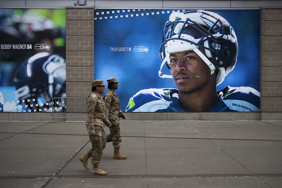 caption: U.S. Army soldiers walk next to a mural of Seahawks wide receiver Tyler Lockett on Tuesday, March 31, 2020, on Occidental Avenue South in Seattle. Soldiers from the 627th Army Hospital from Fort Carson, Colorado, as well as from Joint Base Lewis-McChord set up a 250-bed military field hospital for non COVID-19 patients at the CenturyLink Field Event Center.