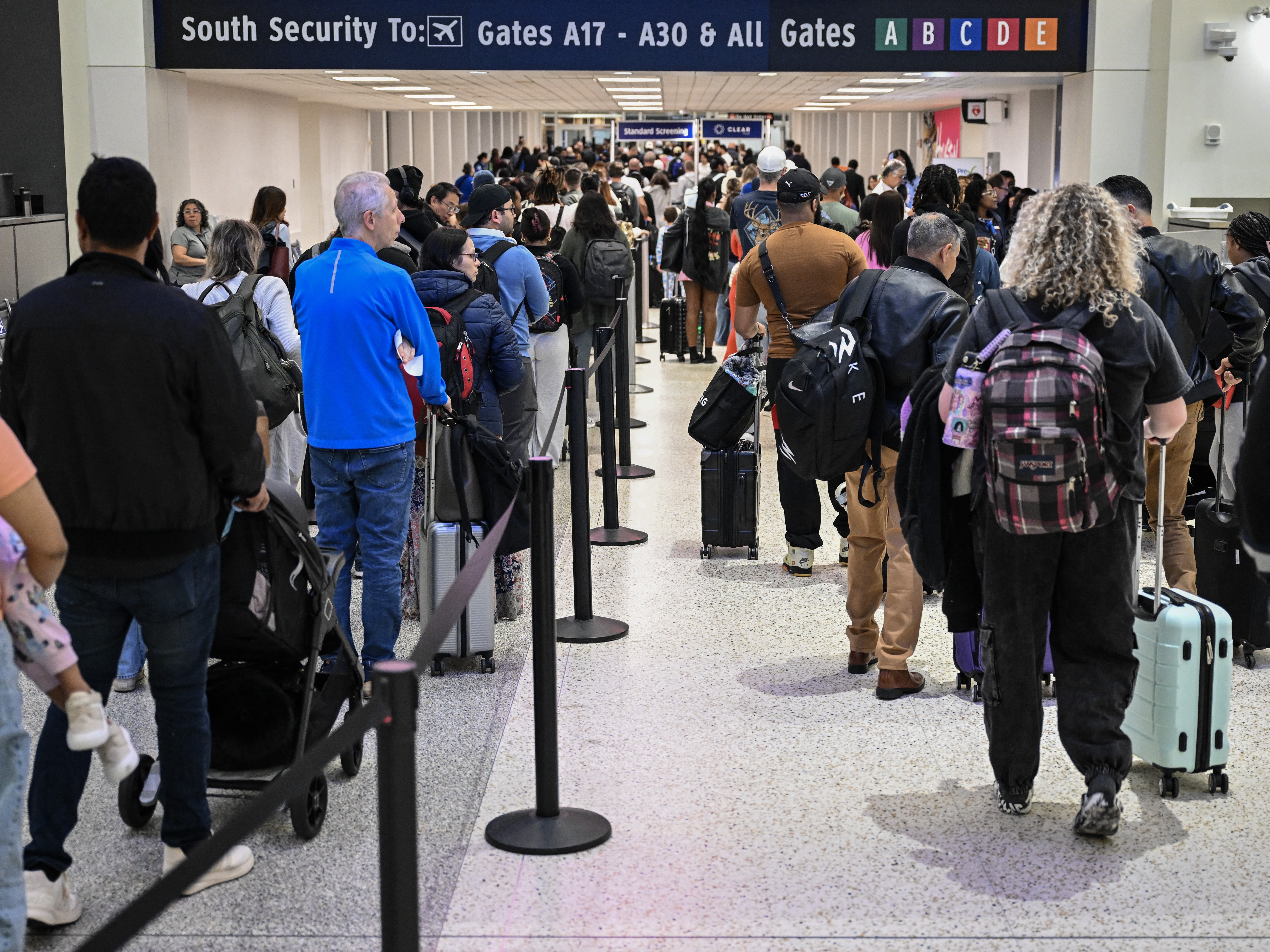 caption: Travelers wait in line at a TSA security checkpoint at George Bush Intercontinental Airport in Houston, Texas, on March 20, 2026.