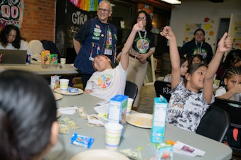 caption: The girls excitedly raise their hands during an activity at Girl Scout Troop 6000's weekly meeting at the Row Hotel on Wednesday evening.