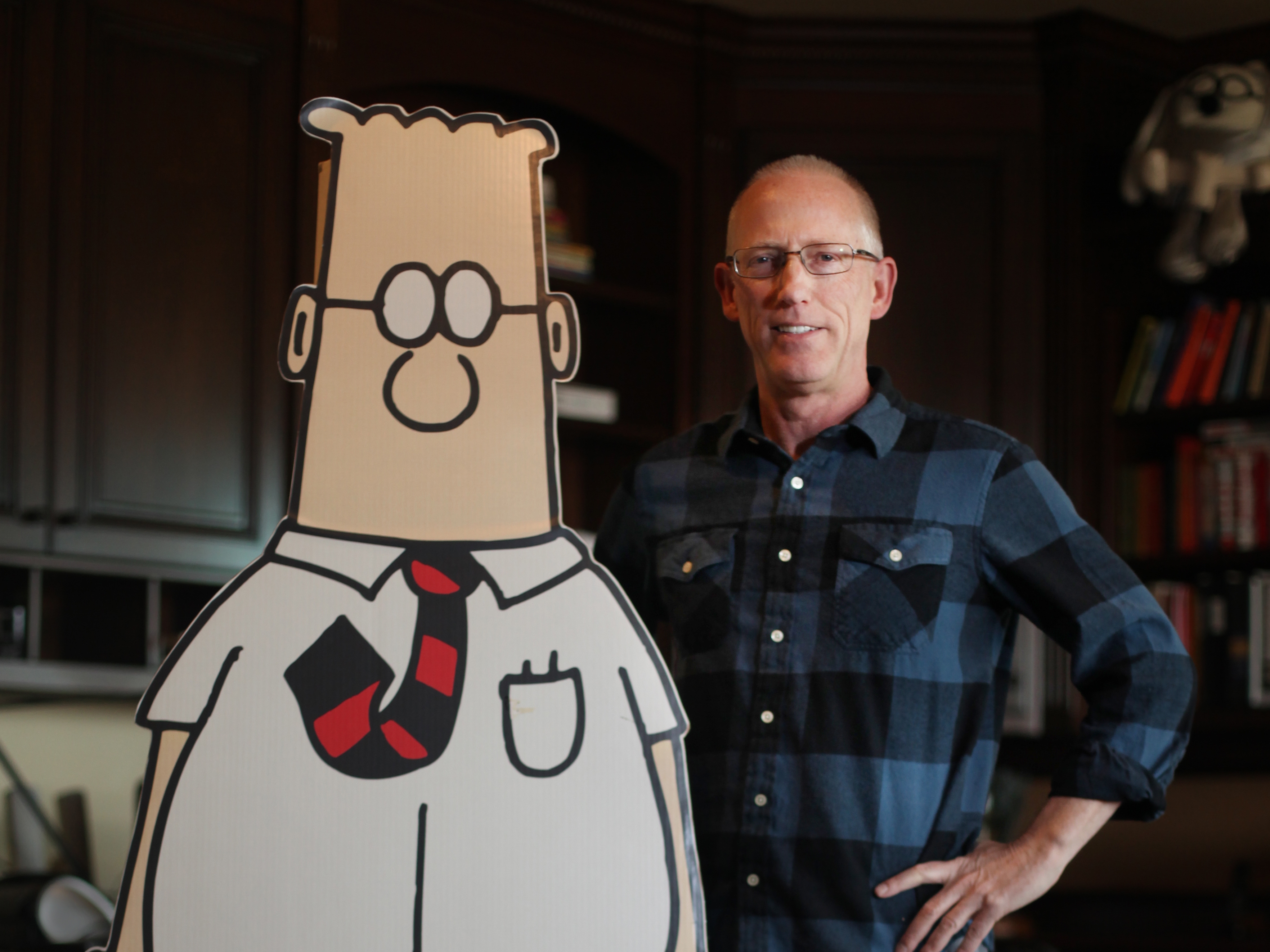 caption: Cartoonist Scott Adams poses with his a life-size cutout of his creation, Dilbert, in 2014.