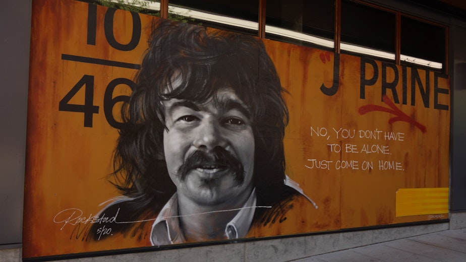caption: A mural of country-folk artist John Prine covers the windows of an apartment building on Pike Street on Capitol Hill. Murals first appeared across the city at the start of the lockdown, but recent protests prompted many more building owners to put up plywood over their street-level windows, providing canvasses for both professional artists and amateurs. John Prine, who passed away on April 7th, was among the first prominent victims of the Covid-19 virus in the United States.