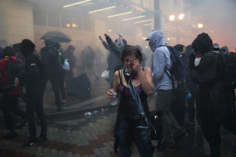 caption: A protester reacts to tear gas near the intersection of 5th and Pine Streets on Saturday, May 30, 2020, in Seattle. Thousands gathered in a protest following the violent  police killing of George Floyd, a Black man who was killed by a white police officer who held his knee on Floyd's neck for 8 minutes and 46 seconds, as he repeatedly said, 'I can't breathe,' in Minneapolis on Memorial Day. 