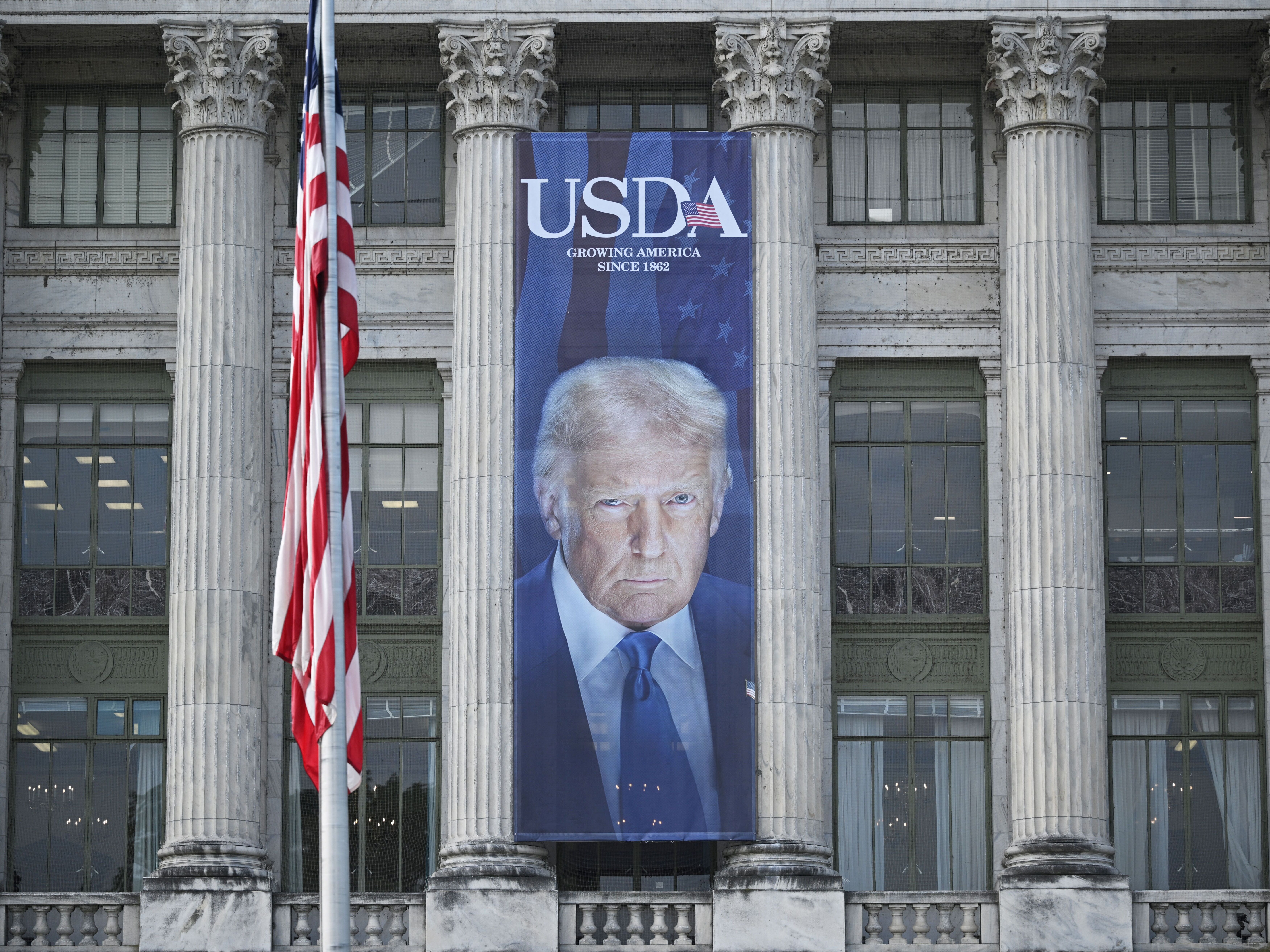 caption: A banner showing an image of US President Donald Trump hangs on the side of a US Department of Agriculture building in Washington, DC, on May 16, 2025. USDA has put on hold a demand that states turn over sensitive data about food assistance recipients.