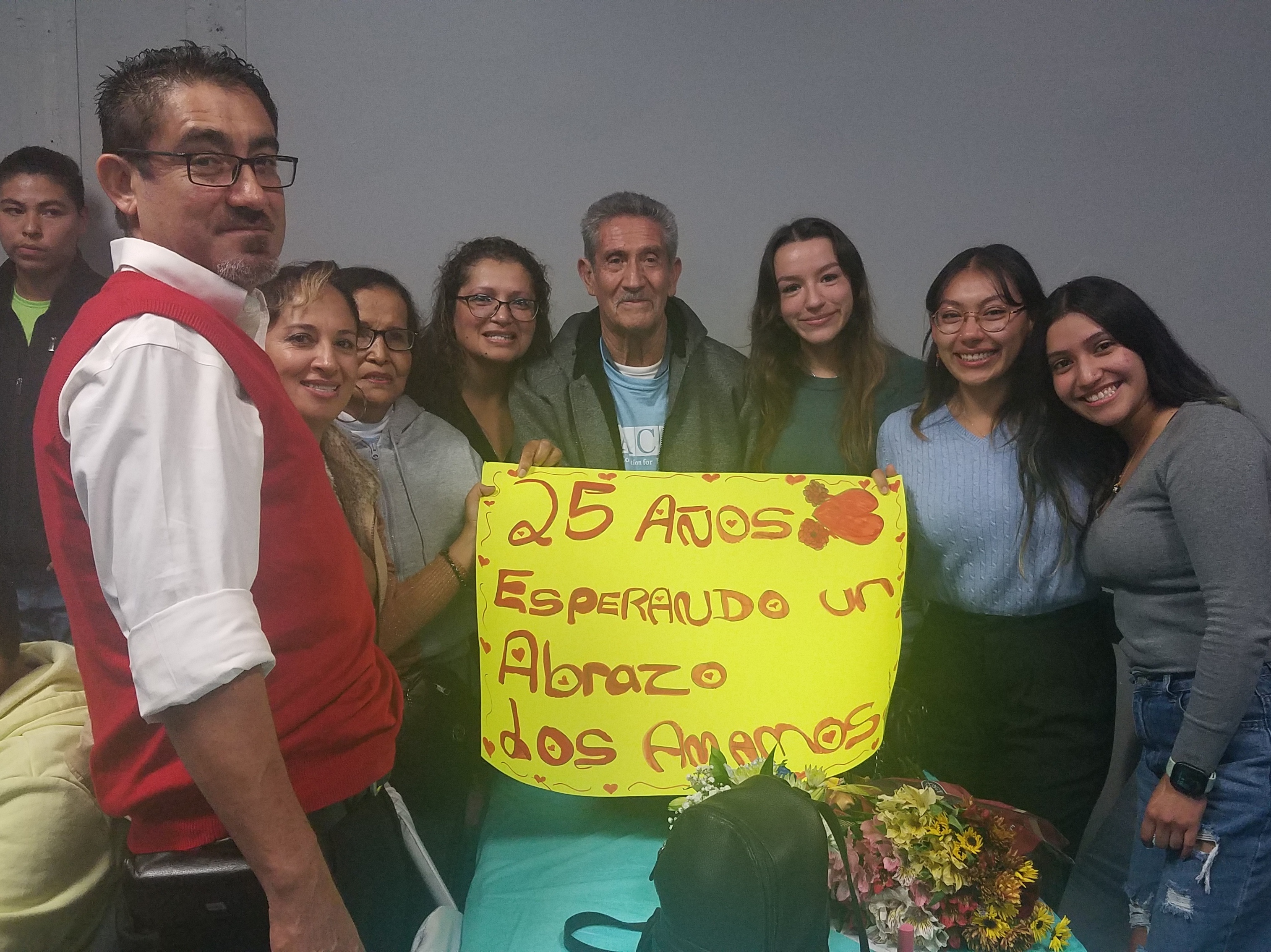 caption: The Rodriguez Tellez family poses for a picture, together for the first time in 25 years. The sign says, "25 years waiting for a hug. We love you."