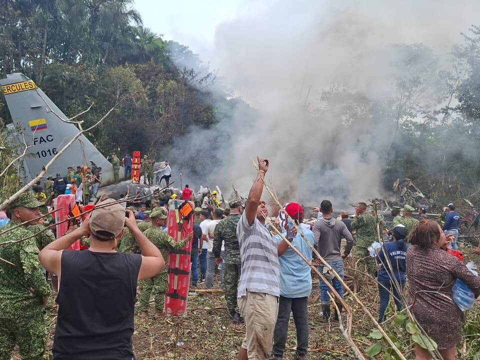 caption: People stand around a military cargo plane that crashed after taking off from Puerto Leguizamo, Colombia, a remote municipality in the Amazonian province of Putumayo, Monday, March 23, 2026.